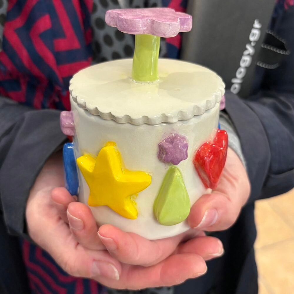 Χέρια κρατούν ένα μοναδικό ανάγλυφο βάζο, αποτέλεσμα δημιουργίας από τα μαθήματα κεραμικής και πηλού στο εργαστήριό μας Theta for Ceramics.